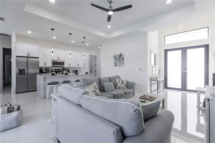 Living area with a tray ceiling, Glass entry double doors, ceiling fan, and recessed lighting