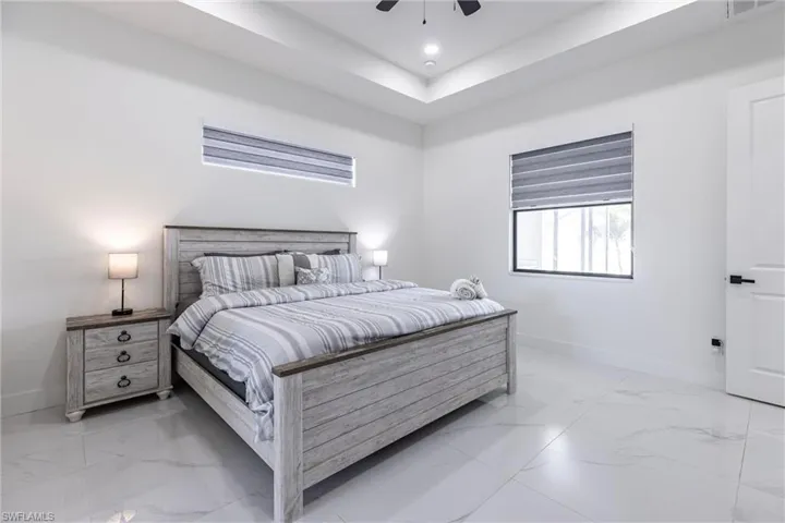 Bedroom with light marble finish floors, a raised ceiling, ceiling fan, and recessed lighting
