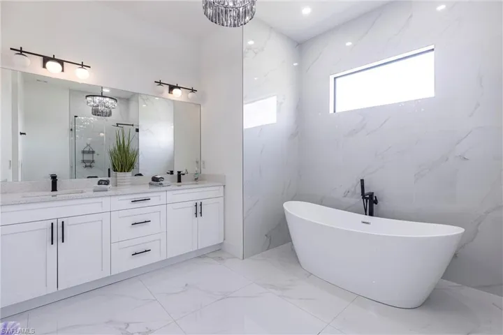 Bathroom with light tile flooring, double vanity, a freestanding bath, a marble finish shower, and a chandelier
