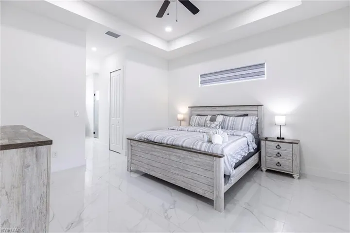 Bedroom with a tray ceiling, light marble finish flooring, ceiling fan, recessed lighting, and a closet