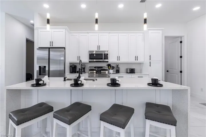 Kitchen with light quartz counters, appliances with stainless steel finishes, white cabinets, a kitchen bar, and recessed lighting