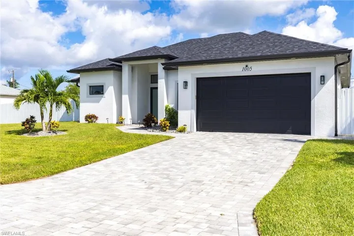 Modern style house with stucco siding, decorative driveway, a front yard, and an attached garage