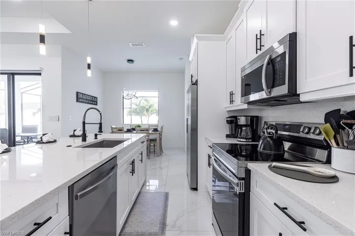 Kitchen featuring stainless steel appliances, white cabinetry, hanging light fixtures, light quartz counters, and recessed lighting