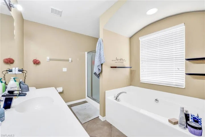 Primary bathroom featuring vanity, a garden tub, light tile patterned floors, and a shower stall