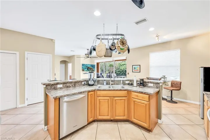 Kitchen featuring stainless steel appliances, a center island with sink, arched walkways, light tile patterned floors, and recessed lighting