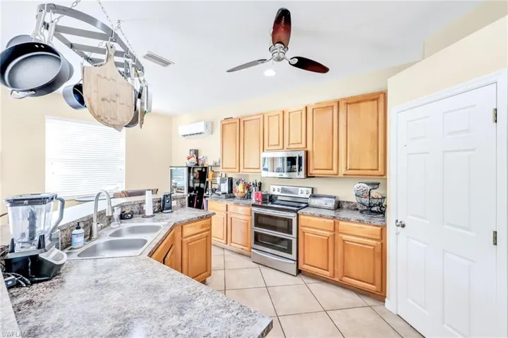 Kitchen with appliances with stainless steel finishes, light tile patterned floors, a ceiling fan, a wall mounted AC, and light brown cabinets