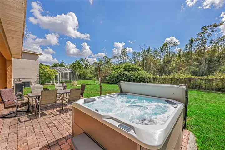View of patio with outdoor dining area, a hot tub, a lanai, and view of wooded area