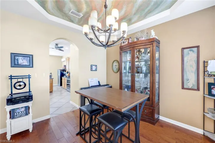 Dining area with arched walkways, hardwood / wood-style floors, a raised ceiling, ceiling fan, and a chandelier