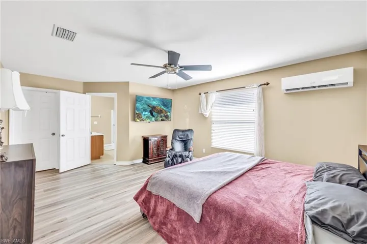 Primary bedroom featuring connected bathroom, light wood-type flooring, a wall mounted air conditioner, and a ceiling fan