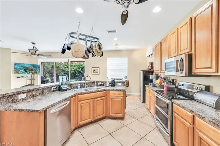 Kitchen featuring a ceiling fan, stainless steel appliances, light tile patterned floors, recessed lighting, and a kitchen island with sink
