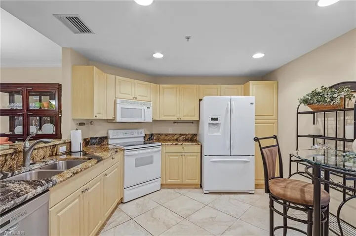 Kitchen featuring dark stone counters, crown molding, white appliances, light tile patterned floors, and sink