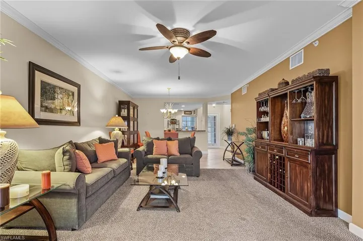 Living room featuring light colored carpet, ornamental molding, and ceiling fan with notable chandelier