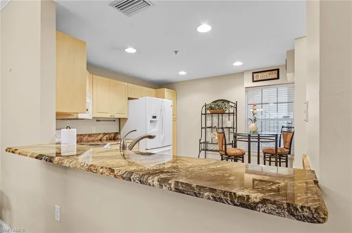 Kitchen featuring white refrigerator with ice dispenser, stone countertops, kitchen peninsula, and sink