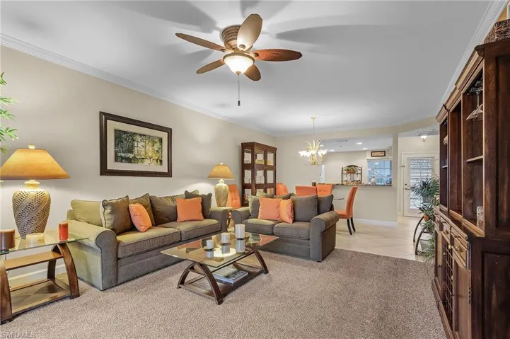 Carpeted living room featuring ceiling fan with notable chandelier and ornamental molding
