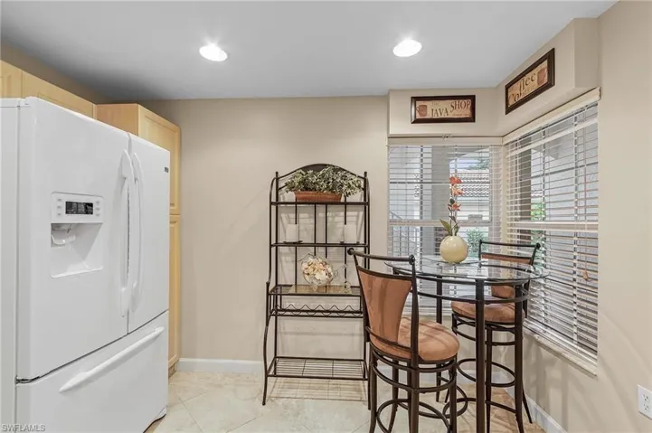 Kitchen with light brown cabinetry, light tile patterned floors, and white fridge with ice dispenser
