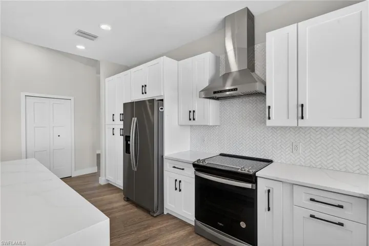 Kitchen with light stone counters, electric range oven, stainless steel fridge, white cabinets, and recessed lighting