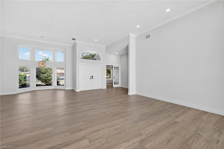 Unfurnished living room featuring healthy amount of natural light, a high ceiling, light wood-type flooring, ornamental molding, and recessed lighting