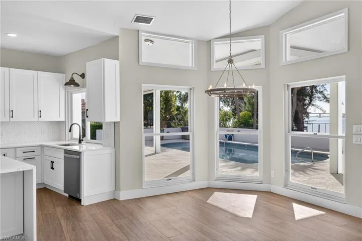 Kitchen with decorative backsplash, hanging lights, light stone counters, white cabinets, and light wood-style floors