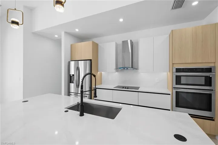 Kitchen with light stone countertops, stainless steel appliances, pendant lighting, wall chimney exhaust hood, and white cabinets