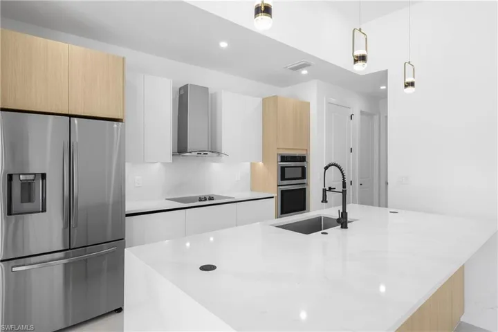 Kitchen featuring wall chimney range hood, a center island with sink, and appliances with stainless steel finishes