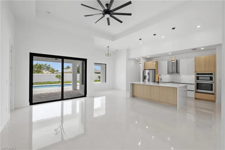 Kitchen with stainless steel appliances, a center island with sink, light tile flooring, wall chimney range hood, and a towering ceiling
