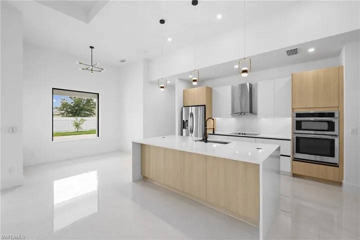Kitchen featuring wall chimney range hood, stainless steel appliances, an island with sink, sink, and light tile floors