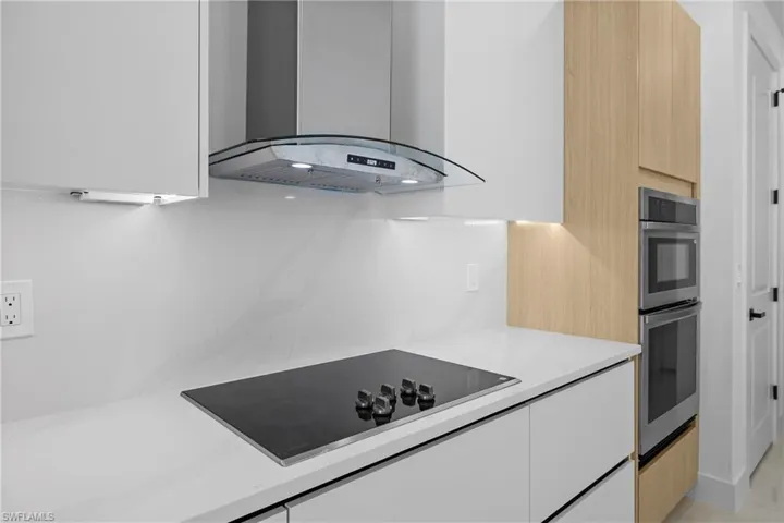 Kitchen featuring light stone countertops, extractor fan, black electric cooktop, white cabinets, and double oven