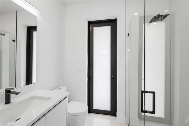 Bathroom featuring tile floors, a shower with door, vanity, and toilet