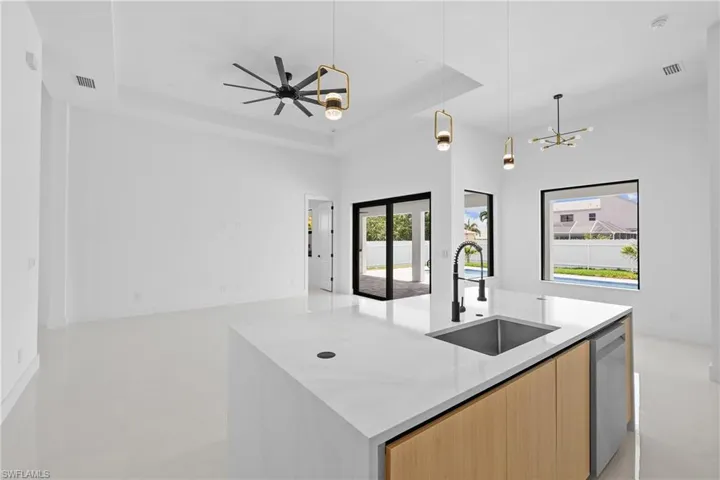 Kitchen featuring dishwasher, a raised ceiling, light tile floors, sink, and a kitchen island with sink