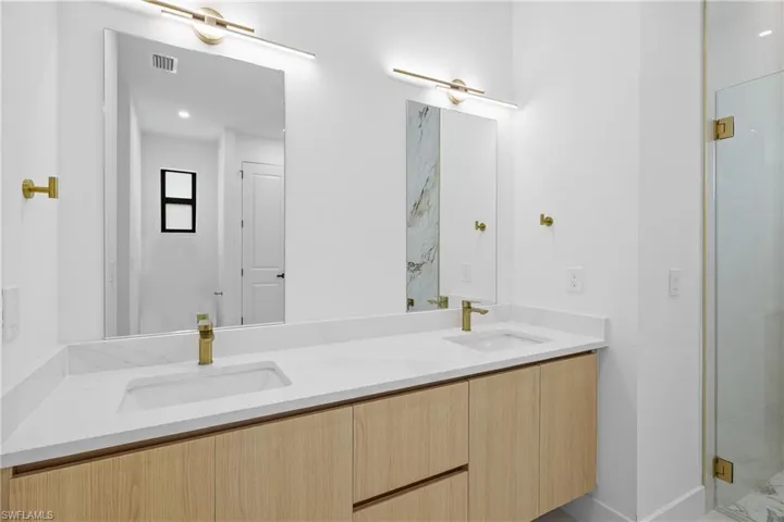 Bathroom with a shower with shower door, oversized vanity, and dual sinks