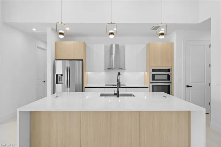 Kitchen with appliances with stainless steel finishes, white cabinets, an island with sink, and wall chimney exhaust hood