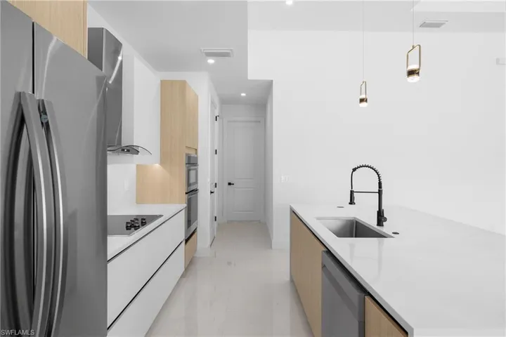Kitchen featuring decorative light fixtures, stainless steel appliances, a center island with sink, sink, and light tile floors