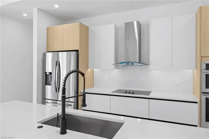 Kitchen with wall chimney range hood, white cabinets, and stainless steel refrigerator with ice dispenser