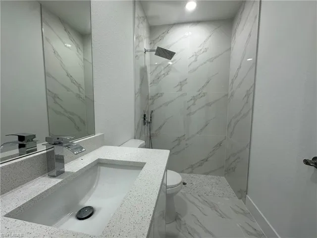 Bathroom featuring tiled shower, tile floors, vanity, and toilet