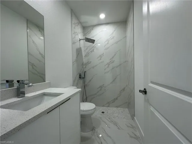 Bathroom with a tile shower, vanity, toilet, and tile floors