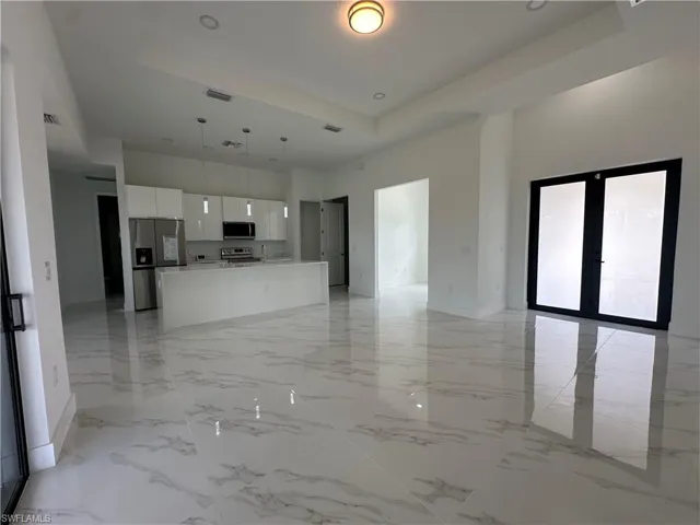 Unfurnished living room with a tray ceiling, french doors, and light tile floors