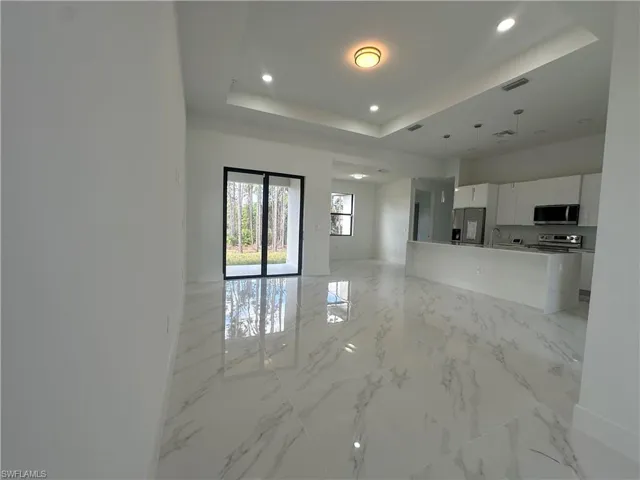 Unfurnished living room featuring a raised ceiling, light tile flooring, and sink