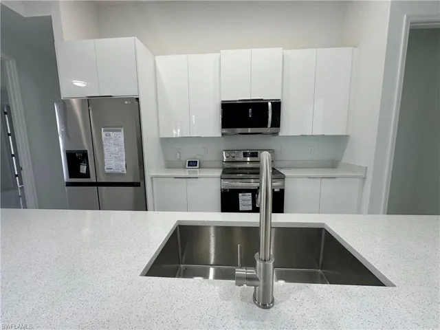 Kitchen featuring appliances with stainless steel finishes, white cabinetry, and light stone counters