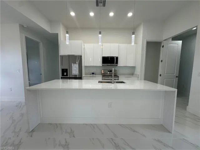 Kitchen featuring appliances with stainless steel finishes, a kitchen island with sink, white cabinets, and light tile flooring