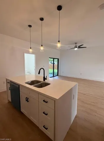 Kitchen featuring white cabinets, pendant lighting, light wood-type flooring, and light stone counters
