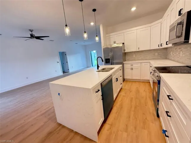 Kitchen with appliances with stainless steel finishes, tasteful backsplash, white cabinets, light stone countertops, and recessed lighting