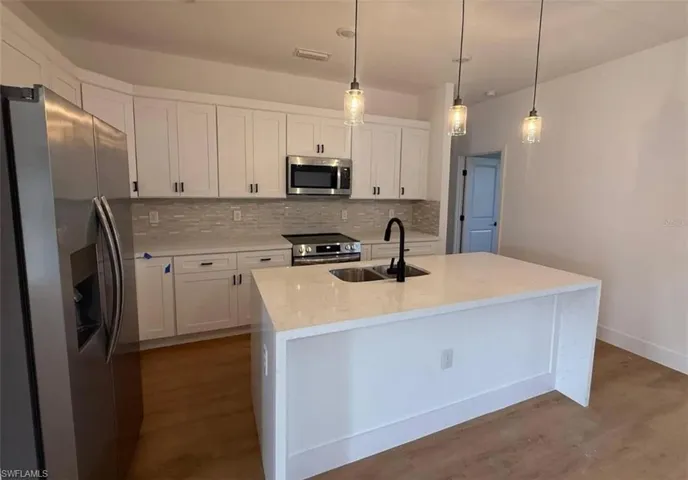 Kitchen featuring appliances with stainless steel finishes, tasteful backsplash, light stone countertops, white cabinets, and decorative light fixtures