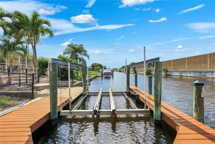 Waterfront property featuring a private boat lift, a composite decking dock, and a fenced yard with mature palm trees