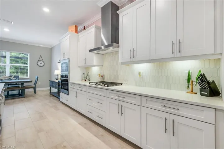 Kitchen with ornamental molding, wall chimney exhaust hood, white cabinetry, tasteful backsplash, and stainless steel appliances