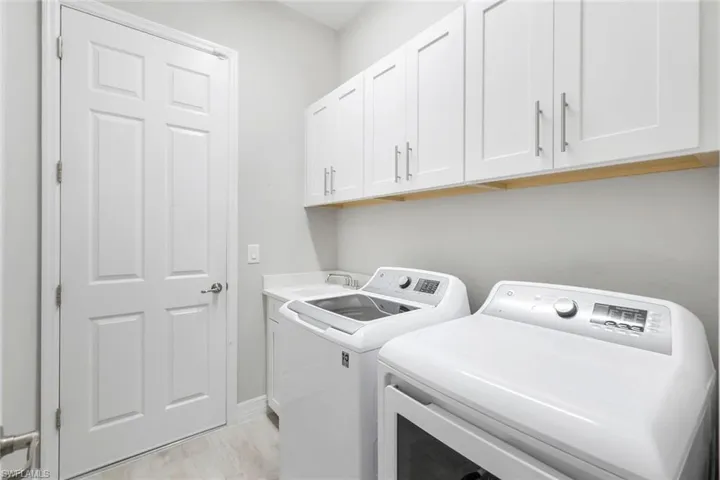 Washroom featuring washer and clothes dryer, cabinet space, and light wood-style floors
