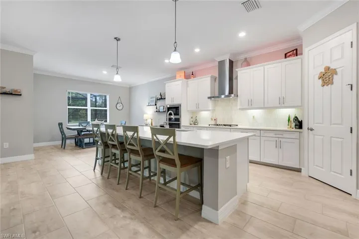Kitchen featuring tasteful backsplash, a kitchen bar, pendant lighting, wall chimney exhaust hood, and white cabinets