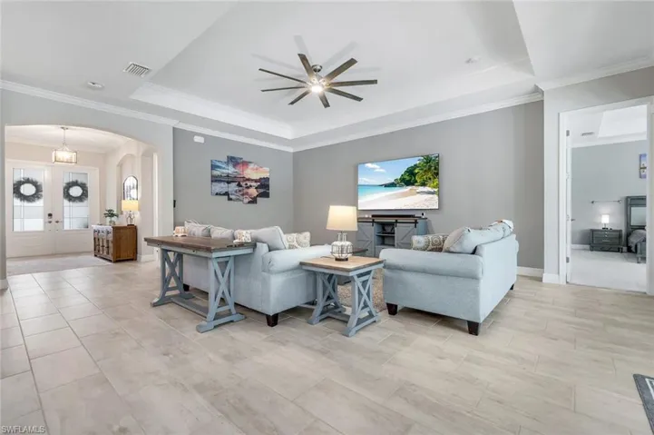 Living room with a tray ceiling, crown molding, arched walkways, a ceiling fan, and french doors