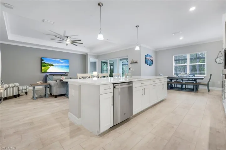 Kitchen featuring white cabinets, hanging light fixtures, ornamental molding, stainless steel dishwasher, and open floor plan