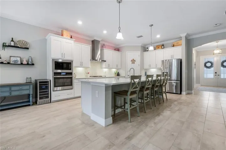 Kitchen featuring tasteful backsplash, appliances with stainless steel finishes, a kitchen bar, a center island with sink, and ornamental molding