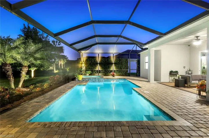 Pool at twilight featuring an outdoor pool, a hot tub, a patio area, and a lanai